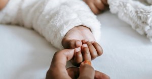 Adult hand extending a finger which is grasped by an infant hand, depicting maternal health. 